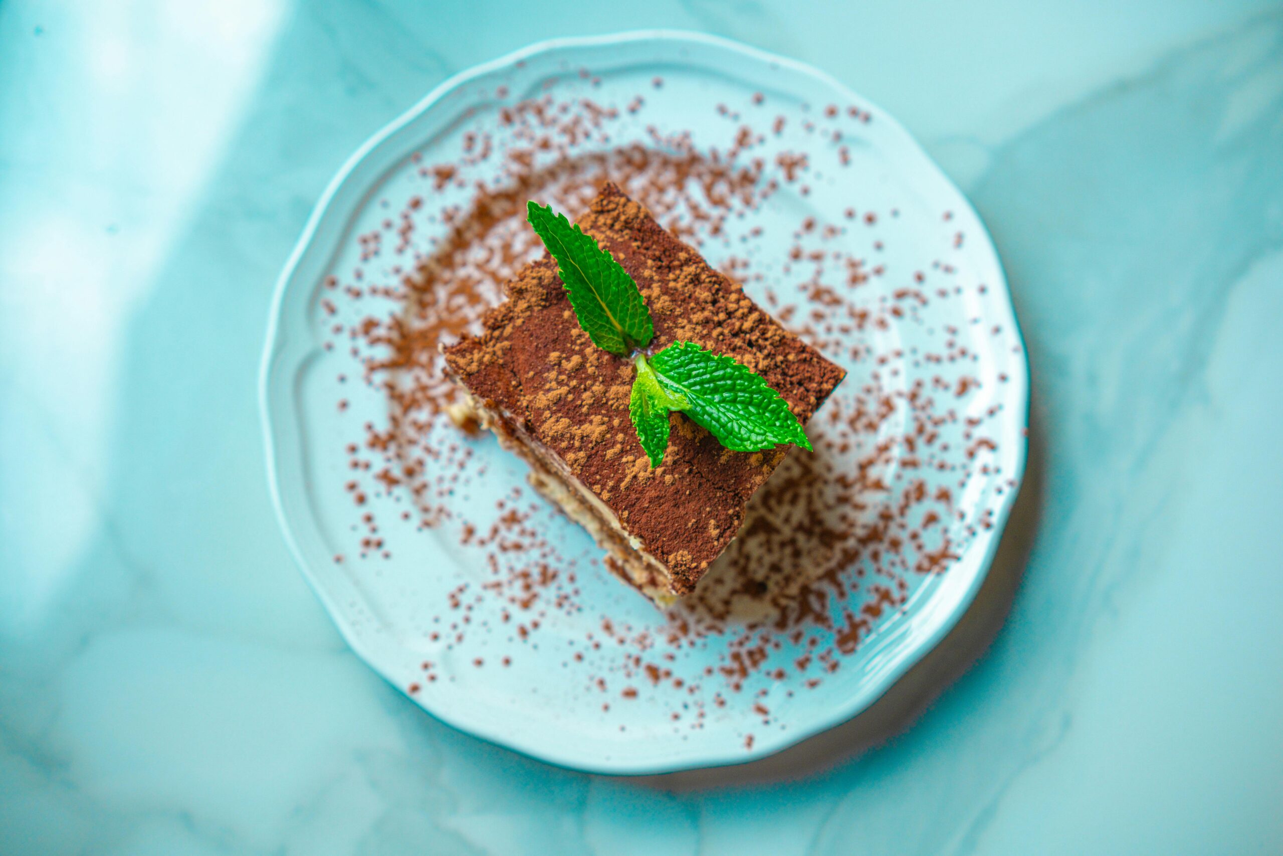 Accueil Indulge in a slice of tiramisu garnished with fresh mint on a classic marble plate.